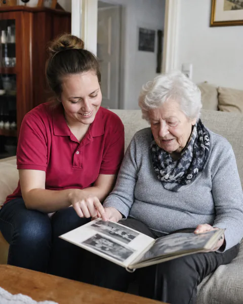 Betreuerin und Seniorin schauen gemeinsam ein Fotoalbum an